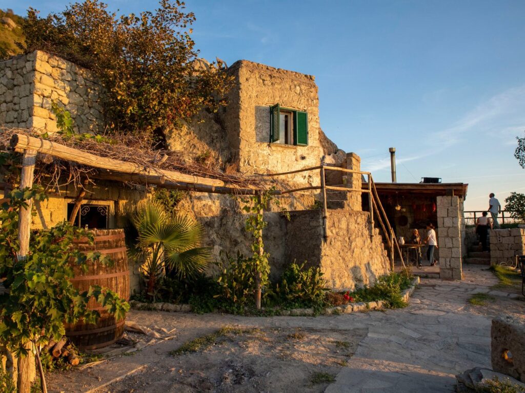 Casa in tufo con persiane verdi, pergolato di canne, una botte e il portico sullo sfondo